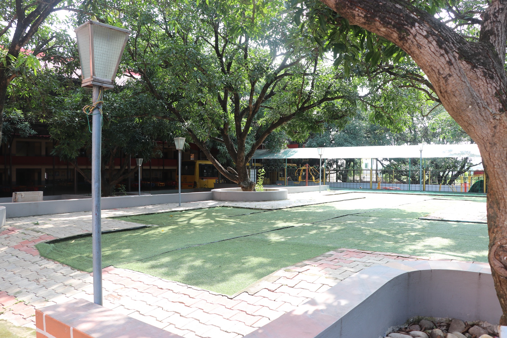 Campus garden with green turf, lampposts and shady trees